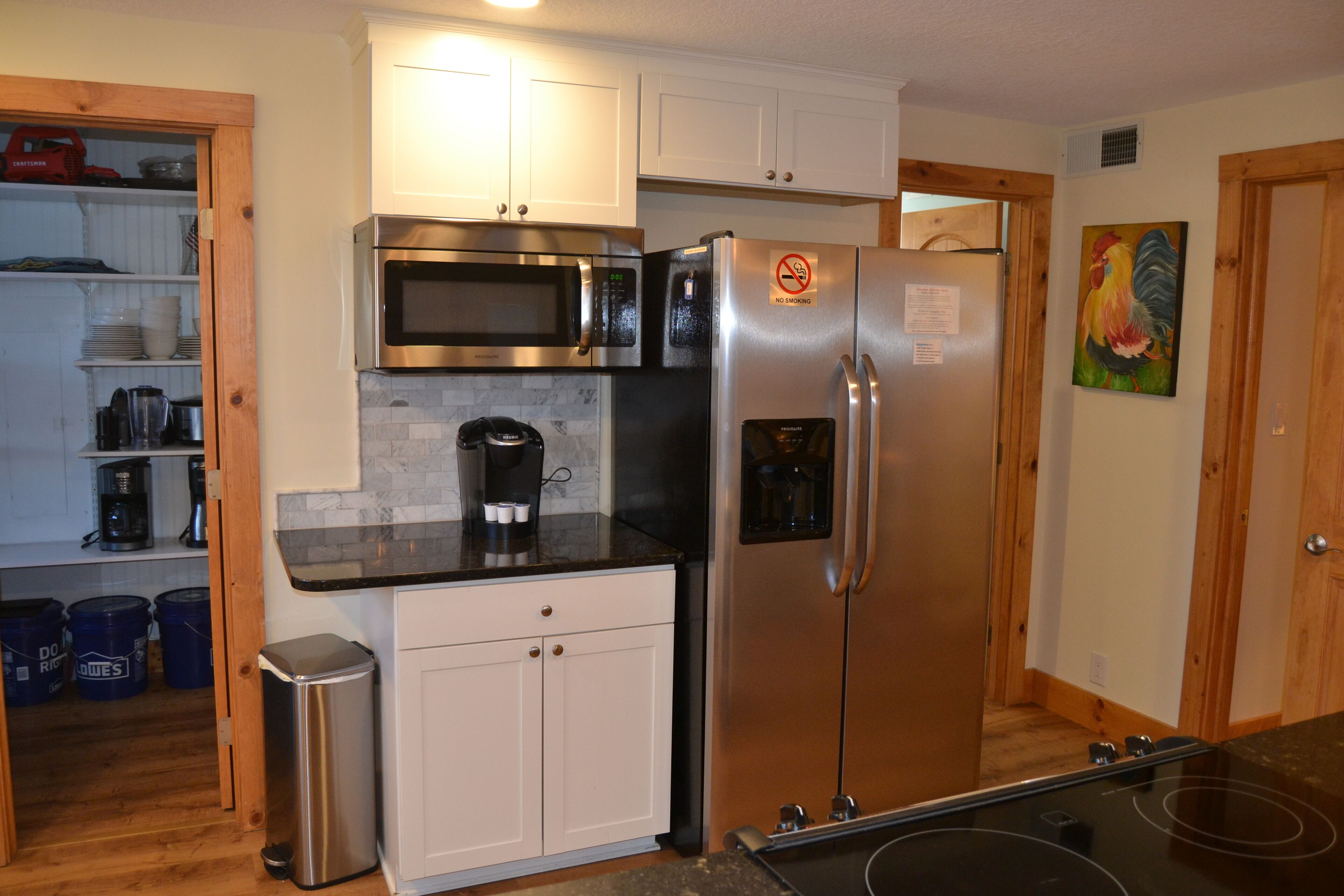 A compact kitchen with a stainless steel refrigerator, microwave, and coffee maker. There are wooden cabinets and a trash can.
