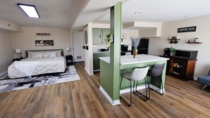 Una habitación de hotel moderna con cama, kitchenette, barra de café y zona de comedor.