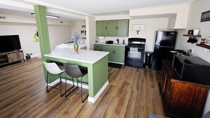 Una cocina moderna con armarios verdes, una isla blanca y un refrigerador negro.