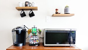 Un espacio para cafetería con una cafetera, un microondas y un armario que contiene cápsulas de café y otros artículos.