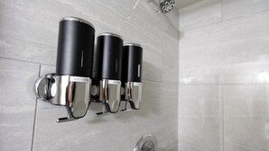 Un baño con tres organizadores de ducha negros y plateados que dicen, de arriba abajo, 'Champú', 'Acondicionador' y 'Gel de baño'.