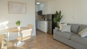 A modern kitchen with white cabinets, a stainless steel refrigerator, and a dining area with a round table and two chairs. - Pier Point (Wildwood)