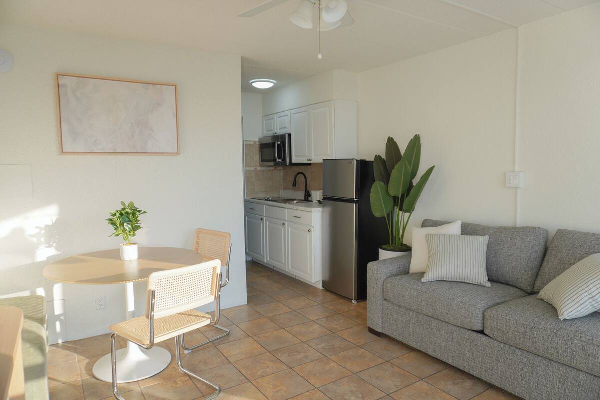 A modern kitchen with white cabinets, a stainless steel refrigerator, and a dining area with a round table and two chairs.