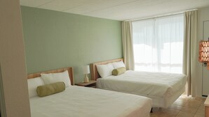 A hotel room with two beds, a nightstand with a lamp, a window with curtains, and a wall-mounted lamp. - Pier Point (Wildwood)