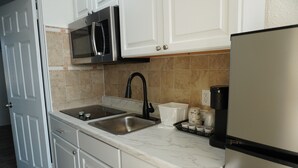 A kitchen with white cabinets, a stainless steel sink, a microwave, and a refrigerator. - Pier Point (Wildwood)