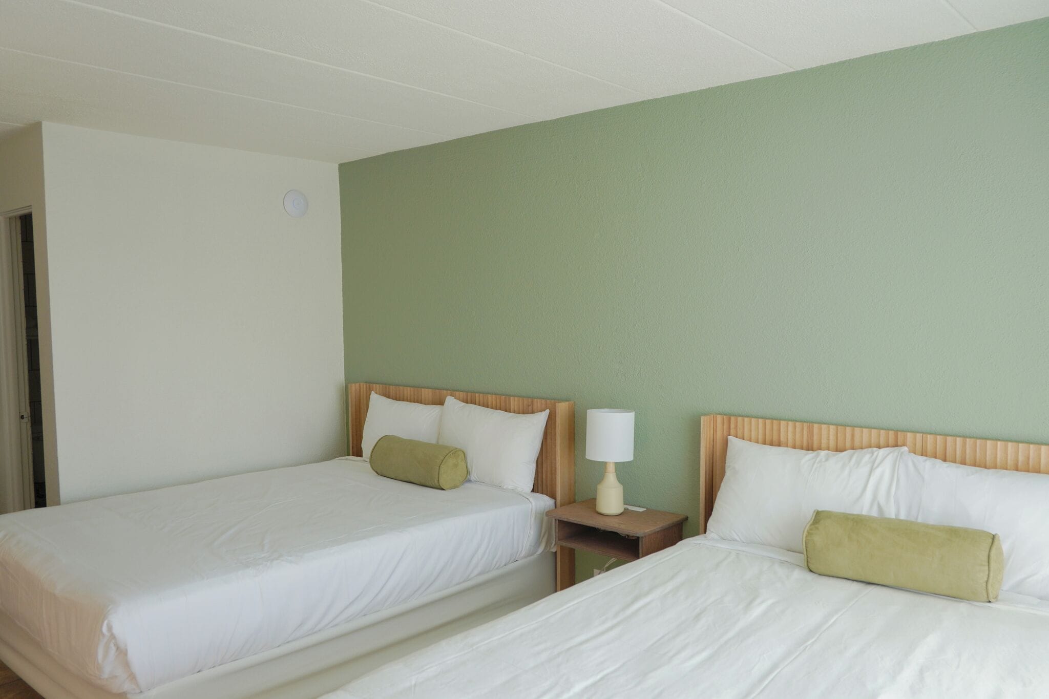 Een hotelkamer met twee eenpersoonsbedden, een nachtkastje met een lamp en een groene accentmuur.