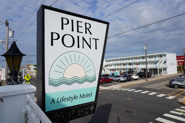 A sign for Pier Point, a Lifestyle Motel, with a view of the street and a building in the background.