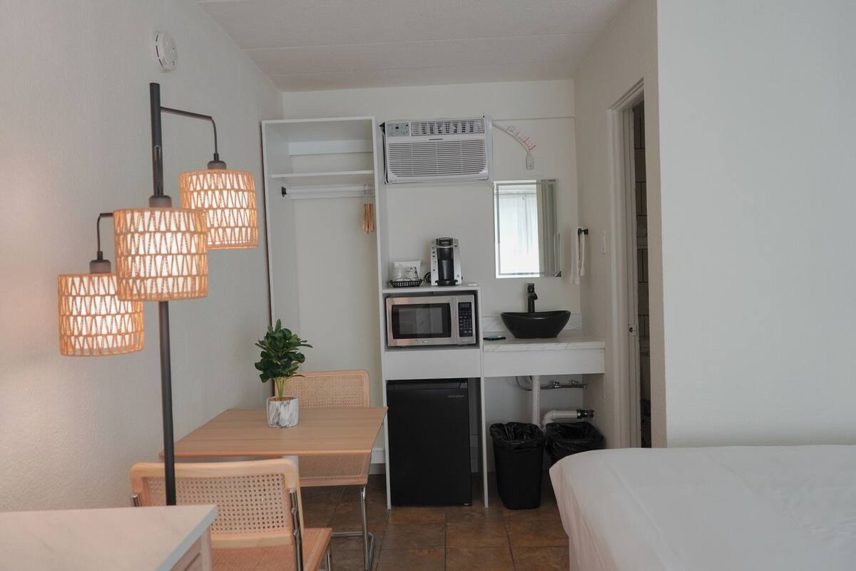 A compact hotel room with a kitchenette, a dining area, and a bed.