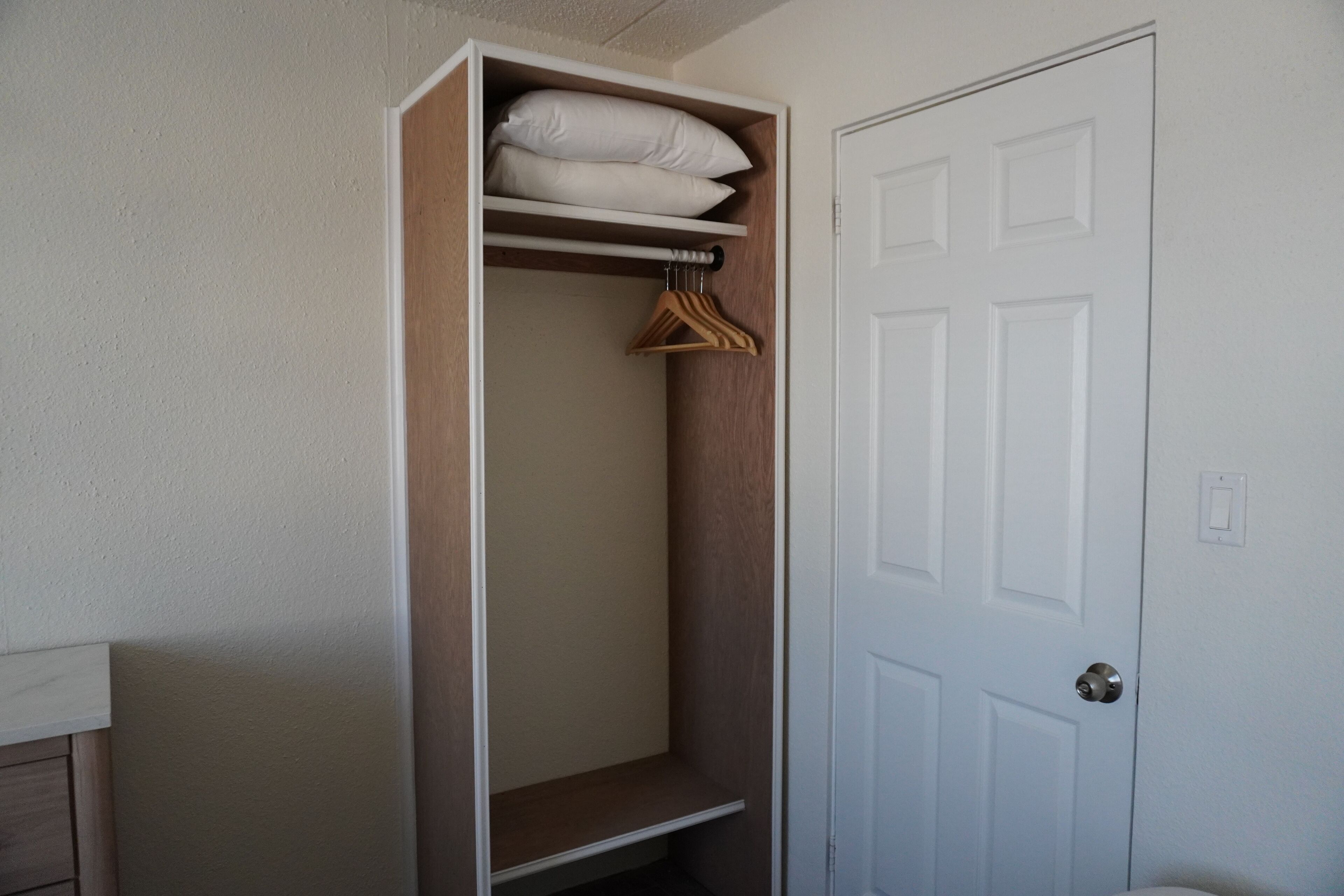 Un dressing avec des étagères et une tringle pour suspendre les vêtements, une porte et un interrupteur sur le mur.