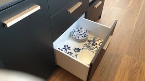 Una cocina con armarios oscuros, un microondas y un cajón con juego de vajilla estampado con motivos florales.