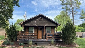 Une petite cabane en bois avec un porche, un espace extérieur couvert aménagé en salon et un petit jardin.
