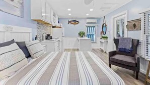 Een compacte, goed verlichte kamer met een kitchenette, een bank, een stoel en een plafondventilator.