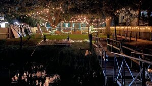 Een nachtzicht van een huis met terras, omgeven door bomen en verlicht met lichtslingers.
