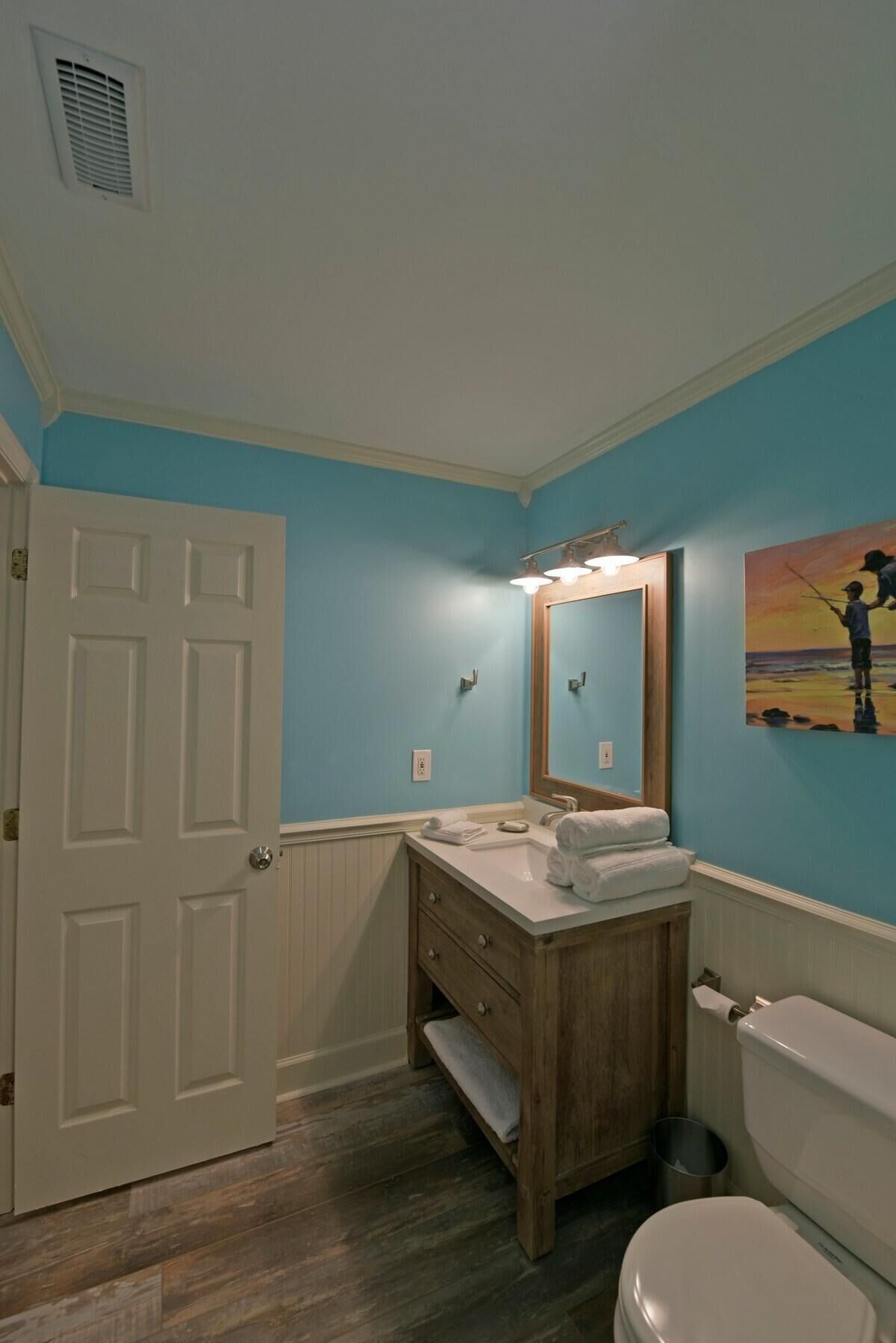 A bathroom with a white toilet, wooden vanity, and a blue wall.