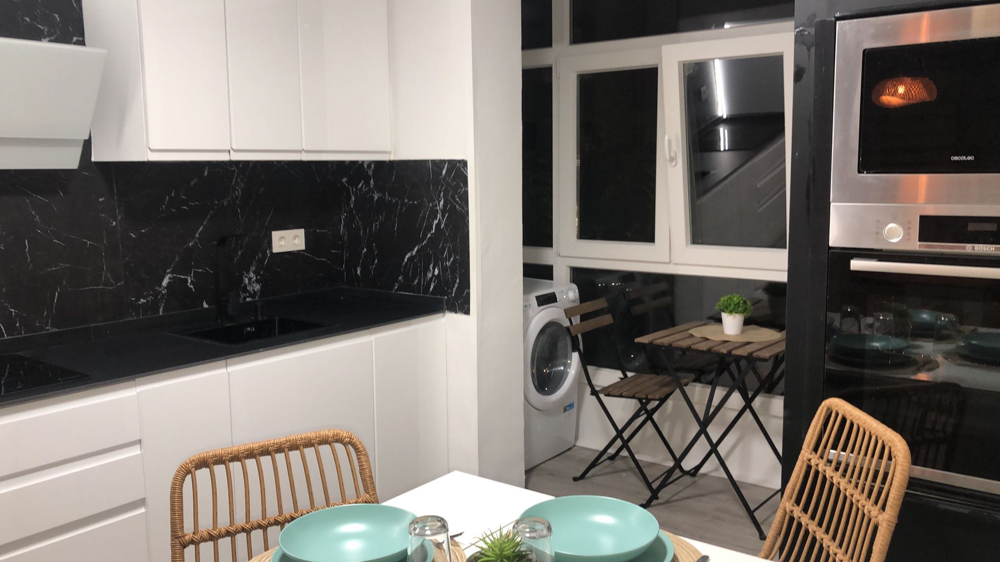 Una cucina compatta con piano di lavoro in marmo nero, lavatrice integrata e forno Bosch.