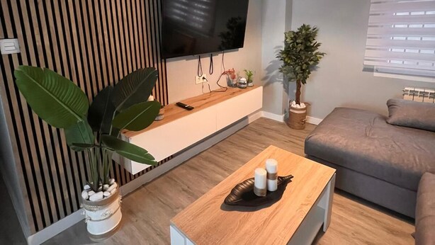 A modern living room with a flat-screen TV mounted on a wall, a wooden coffee table, a grey sofa, and a hanging light fixture. - Apartment in the Arena area of Gijon, near the beach of San Lorenzo.  (Gijón)