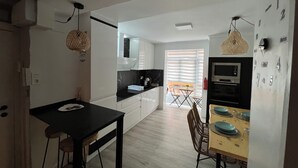 A modern kitchen with white cabinets, a black countertop, and a dining area with a wooden table and chairs. - Apartment in the Arena area of Gijon, near the beach of San Lorenzo.  (Gijón)