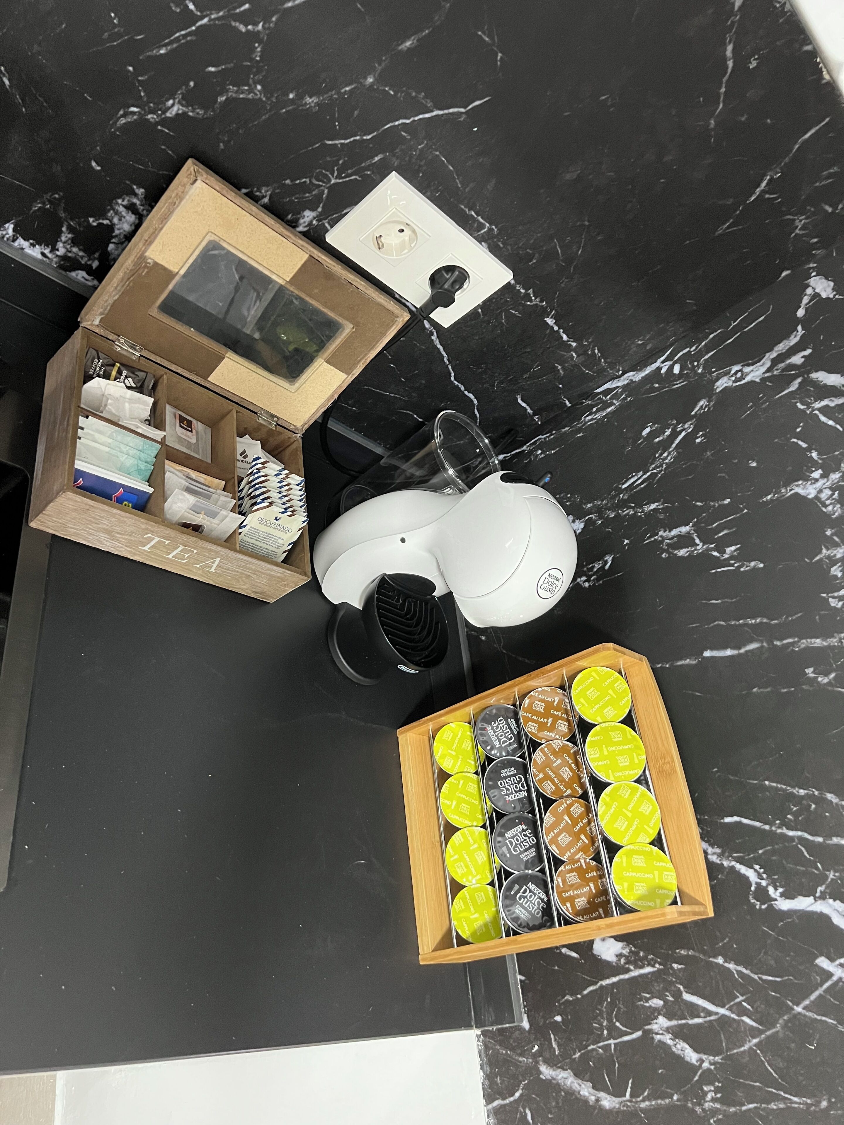 A coffee machine, a box with coffee pods, and a wooden box with various items on a black marble surface.