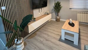 A modern living room with a flat-screen TV mounted on a wall, a wooden accent wall, a white console table, a small wooden coffee table, a hanging pendant light, and a potted plant. - Apartment in the Arena area of Gijon, near the beach of San Lorenzo.  (Gijón)