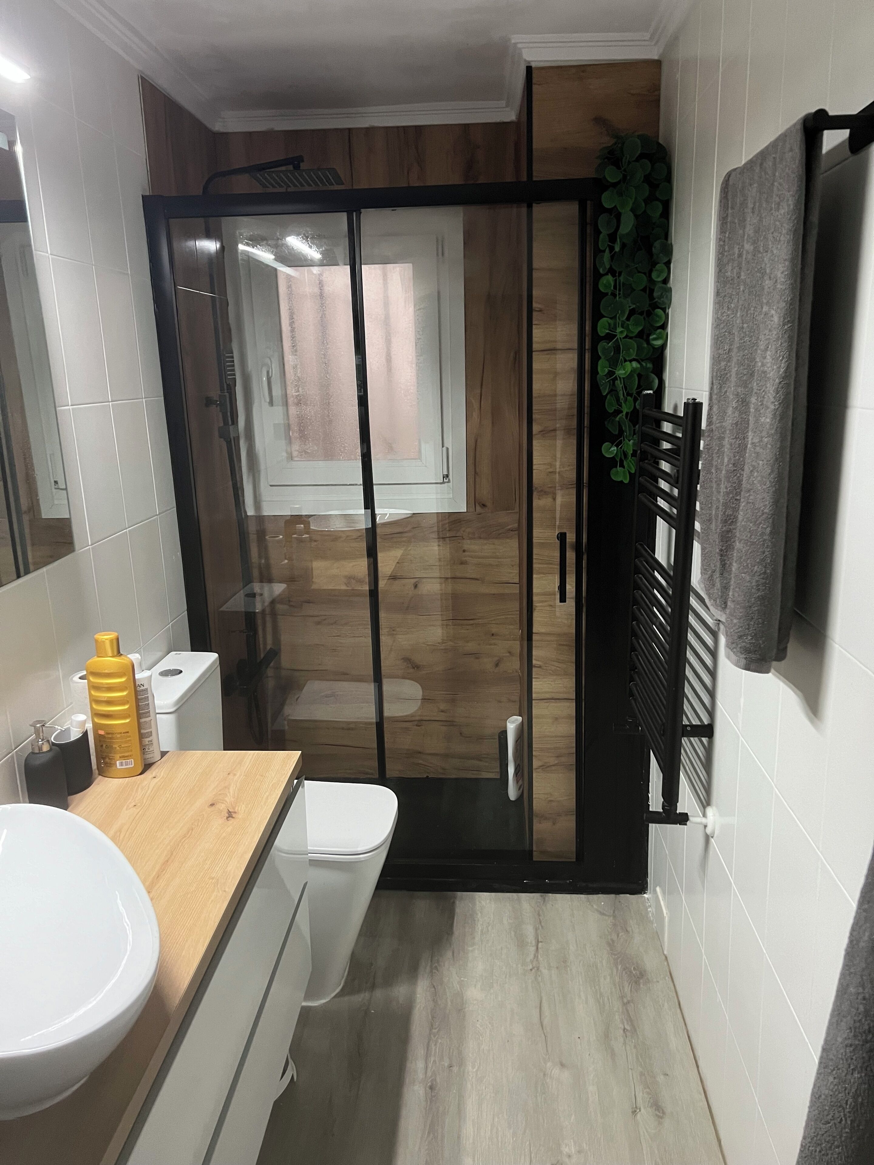 Een moderne badkamer met een douchecabine van glas, een houten wastafelmeubel, een witte wastafel en een handdoekrek.