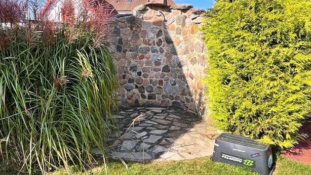 A stone-built outdoor area with a stone wall, a pathway, and a small garden with grass and plants. - stayMA Apartment HeiterKite relax surf fishing, 10m from the Baltic Sea (Wiek)