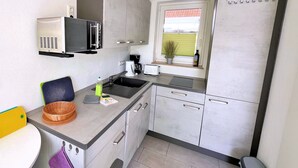 A compact kitchen with a microwave, sink, and a window with a view of a building. - stayMA Apartment HeiterKite relax surf fishing, 10m from the Baltic Sea (Wiek)