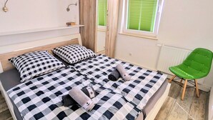A bedroom with a checkered bedspread, a green chair, a mirror, and a window with blinds. - stayMA Apartment HeiterKite relax surf fishing, 10m from the Baltic Sea (Wiek)