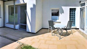 A patio with a table and chairs, a sliding glass door, and a small window with blinds. - stayMA Apartment HeiterKite relax surf fishing, 10m from the Baltic Sea (Wiek)