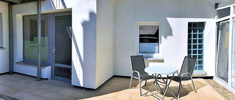 Eine Terrasse mit Tisch und Stühlen, eine Glastür und ein kleines Fenster mit Jalousien.