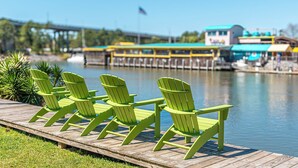 A wooden dock with green Adirondack chairs facing a body of water.