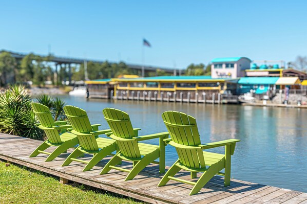 A wooden dock with green Adirondack chairs facing a body of water.