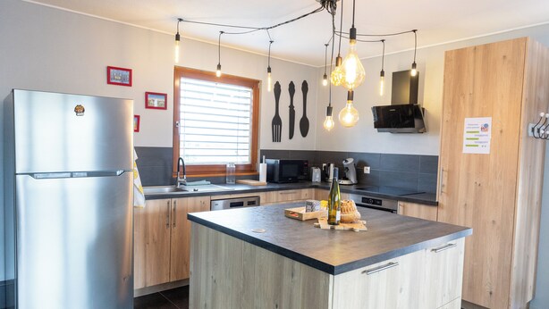 Una cocina moderna con refrigerador de acero inoxidable, armarios de madera, una isla central e iluminación colgante.