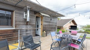 Un patio exterior con una mesa, sillas, una parrilla y una construcción de madera con puerta corrediza.