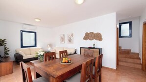 A modern living room with a wooden dining table, a sofa, and a staircase leading to an upper floor.
