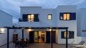 A modern two-story building with a covered patio area, a fireplace, and a dining table.