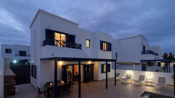 A modern two-story building with a covered patio area, outdoor seating, and a dining area.