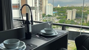 A dining area with a table set for two, a wine bottle, and a glass. The room has a view of a cityscape with buildings and greenery. - Studio Executivo 230m do metro Brooklin (São Paulo)