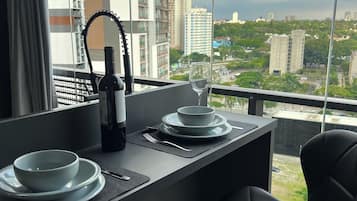Uma área de refeições com uma mesa posta para dois, uma garrafa de vinho e um copo. O ambiente oferece vista para um horizonte urbano com edifícios e áreas verdes.