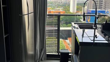 Uma cozinha compacta com geladeira de aço inoxidável, pia e vista para o horizonte urbano através de amplas janelas.