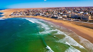 Vue aérienne d’une ville côtière avec une plage, des bâtiments et un ciel dégagé.