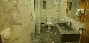 A bathroom with a marble floor, a glass shower enclosure, a toilet, a sink with a mirror, and a hairdryer mounted on the wall. - Hotel Sahara Beach (El Ouatia)