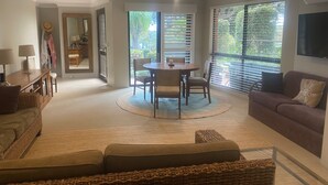 A spacious living area with a round dining table, a sofa, and a TV mounted on the wall. - The Lakeside Garden (Forster)