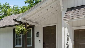 A white house with a dark brown front door, a small porch with steps, and a mailbox.