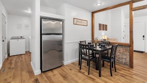 A modern kitchen with a stainless steel refrigerator, a dining table with chairs, and a brick accent wall.