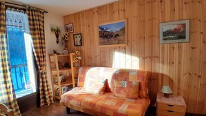 Une pièce chaleureuse avec un mur en bois, un lit, une table de chevet, une chaise en bois et une fenêtre avec des rideaux.