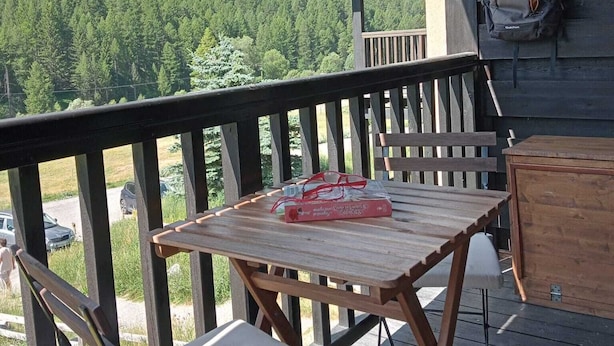 Une terrasse en bois avec une table et des chaises, offrant une vue sur une chaîne de montagnes boisée.