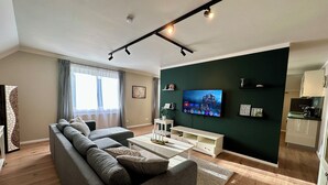 Un salon moderne avec un canapé gris, un téléviseur à écran plat fixé au mur et un plancher en bois.