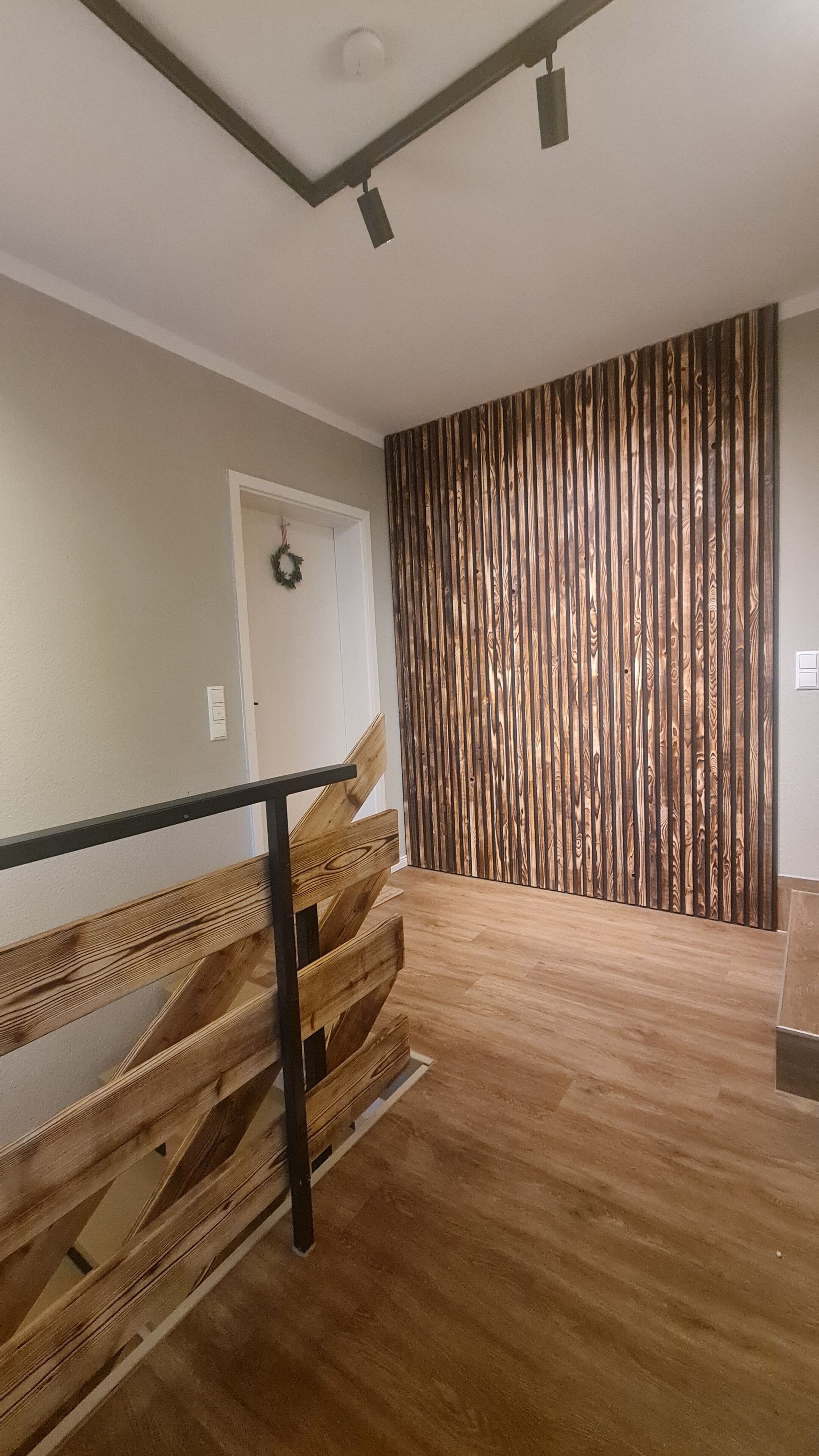 Een kamer met een houten trap, een wand van verticale houten panelen en een lichtschakelaar aan de muur.
