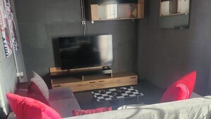 A modern living room with a sofa, red cushions, a TV on a wooden stand, and a checkered table. - jim vila (Andravida)