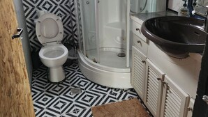 A bathroom with a geometric patterned floor, a white toilet, a glass-enclosed shower, and a black sink. - jim vila (Andravida)